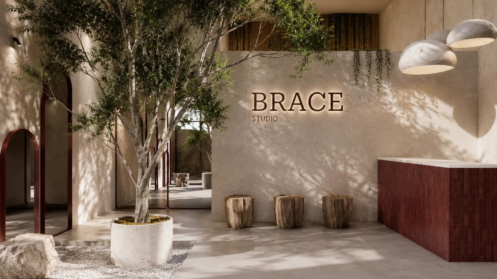 Lobby de Brace Studio: muro de travertino con la señalética retroiluminada BRACE STUDIO, árbol interior y barra de recepción en azulejo granate.